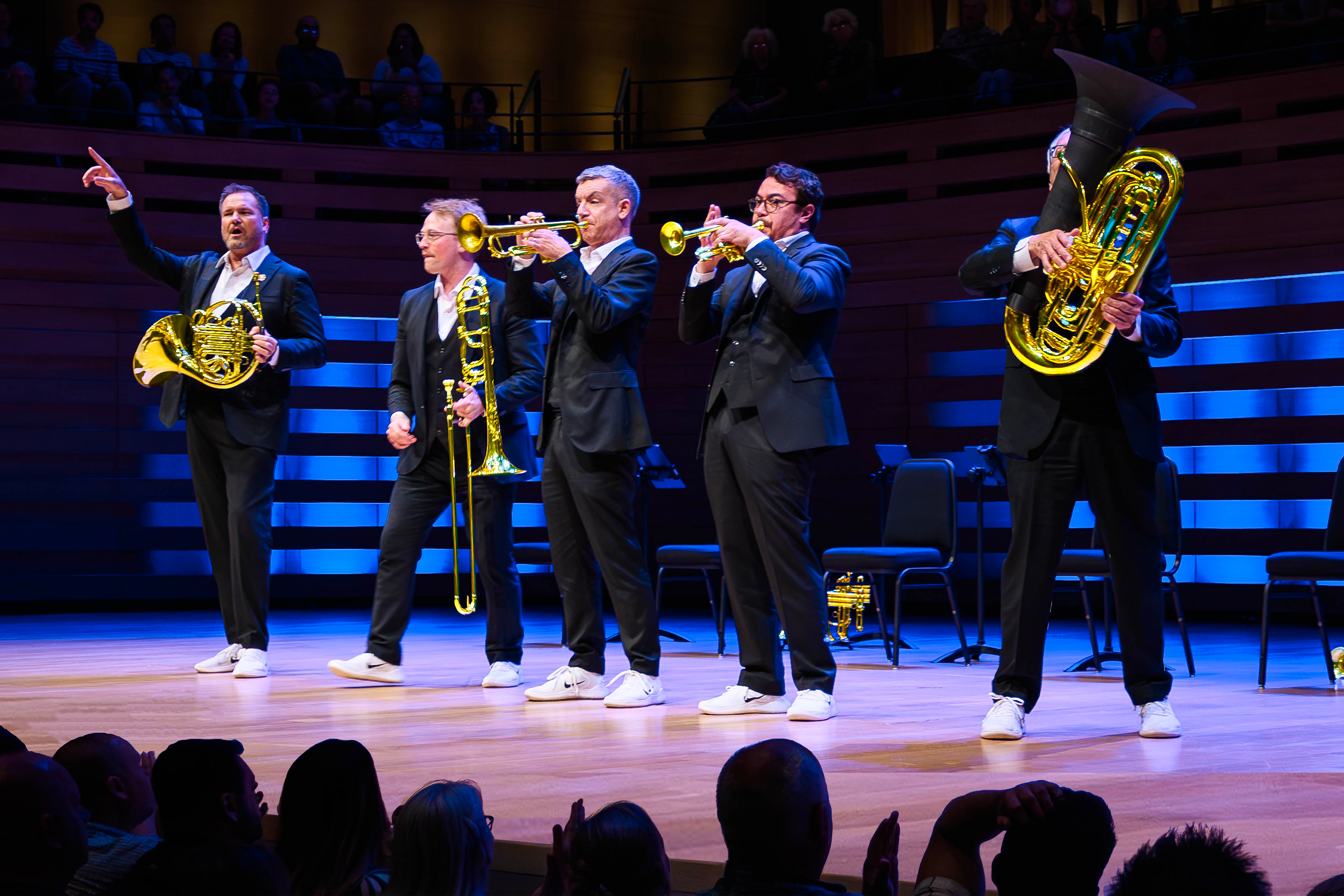 Picture of five men in suits against a black and blue background, holding brass instruments